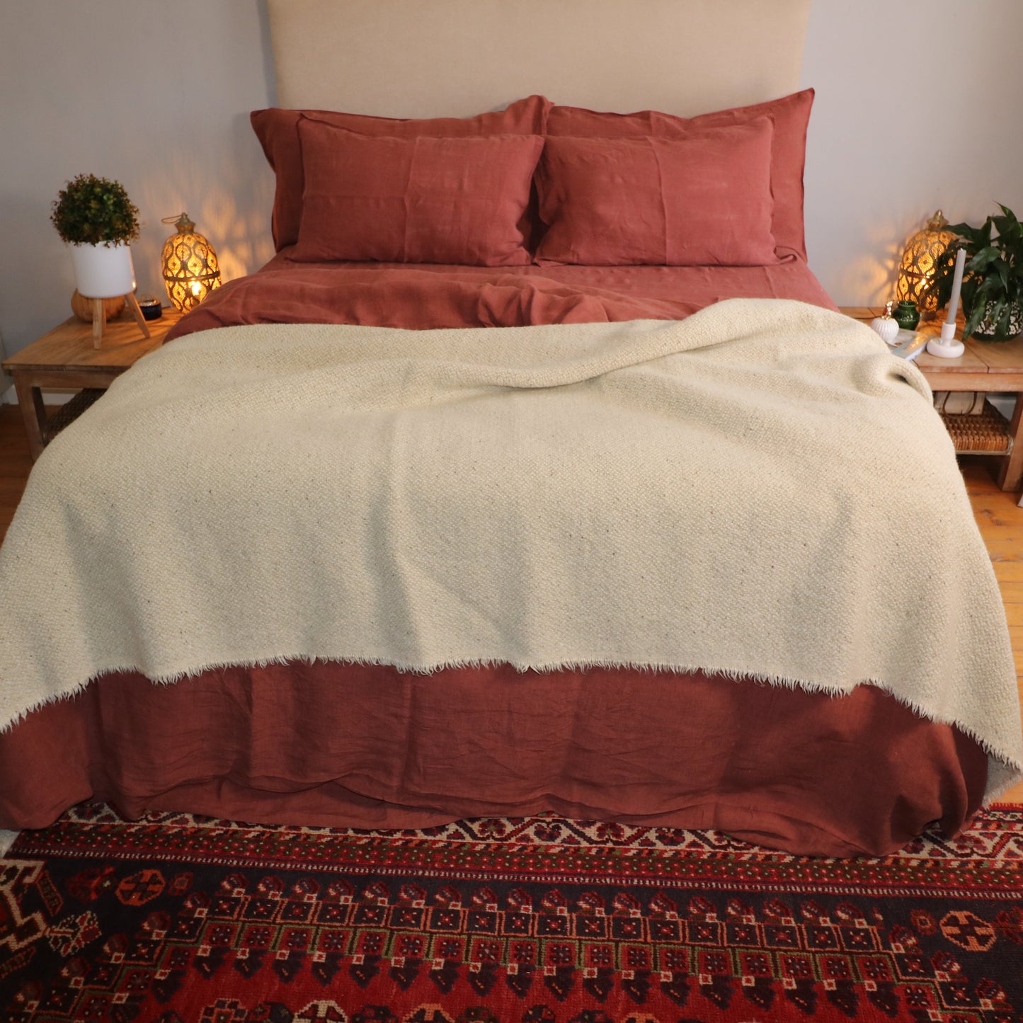 Bedroom with a bed covered in rust bedding and a beige wool blanket, nightstands with lamps, and decorative items.